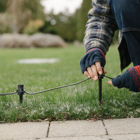 An installer with gloved hands pitches stakes into a lawn
