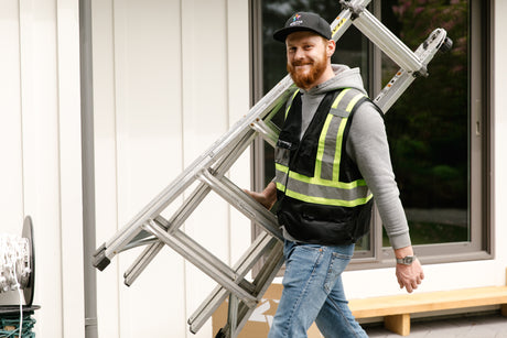 Professional Christmas light installer wearing a safety vest holds a ladder