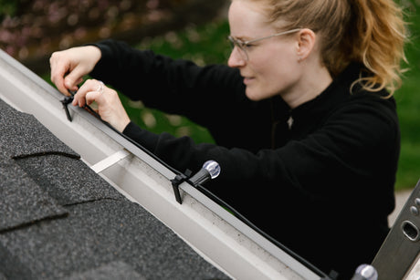 Woman bulbing G30 Christmas lights to gutter black wire